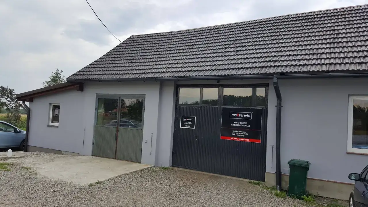 Budynek warsztatu samochodowego z szarym dachem i drzwiami garażowymi z logo "maxserwis".
