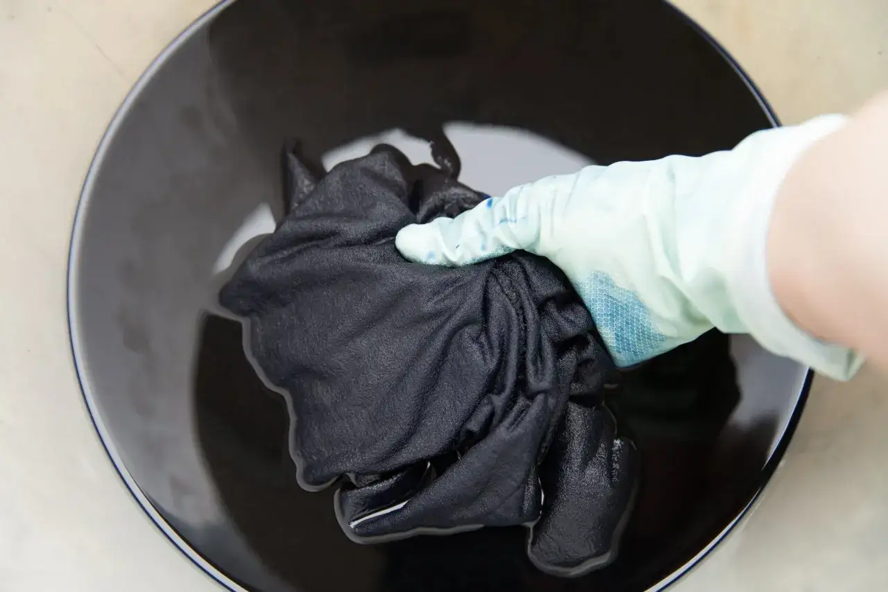 Mano con guante sumerge ropa blanca desteñida de negro en tinte oscuro.