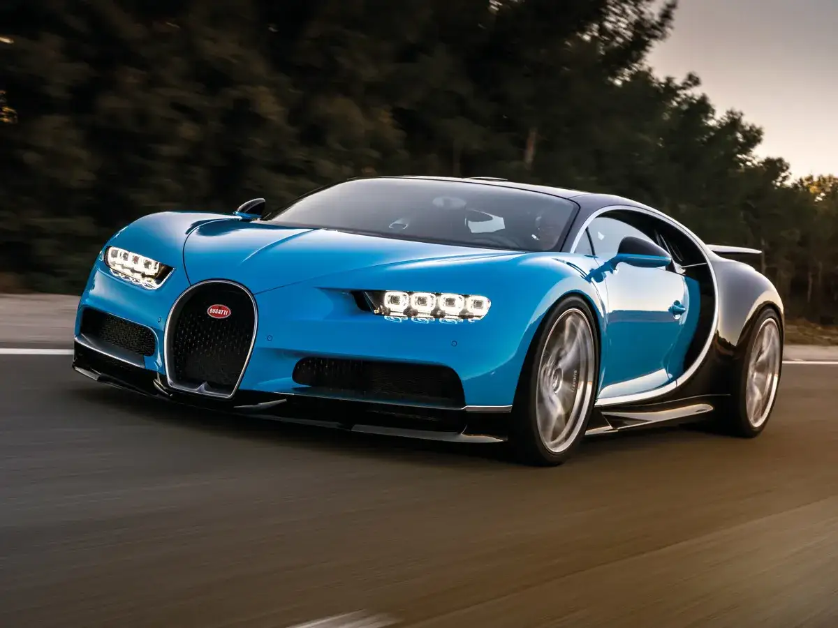 Niebieski Bugatti Chiron pędzi po drodze. Jego cena jest astronomiczna, ale wrażenia z jazdy bezcenne.