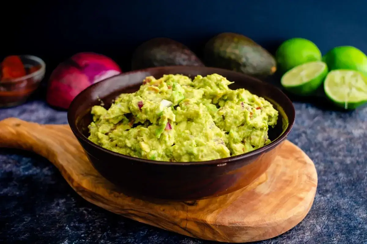 Miseczka guacamole z kawałkami cebuli i limonki w tle.
