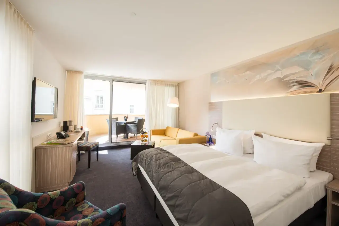 Modernes Hotelzimmer mit Doppelbett, Sofa, Schreibtisch und Balkon.