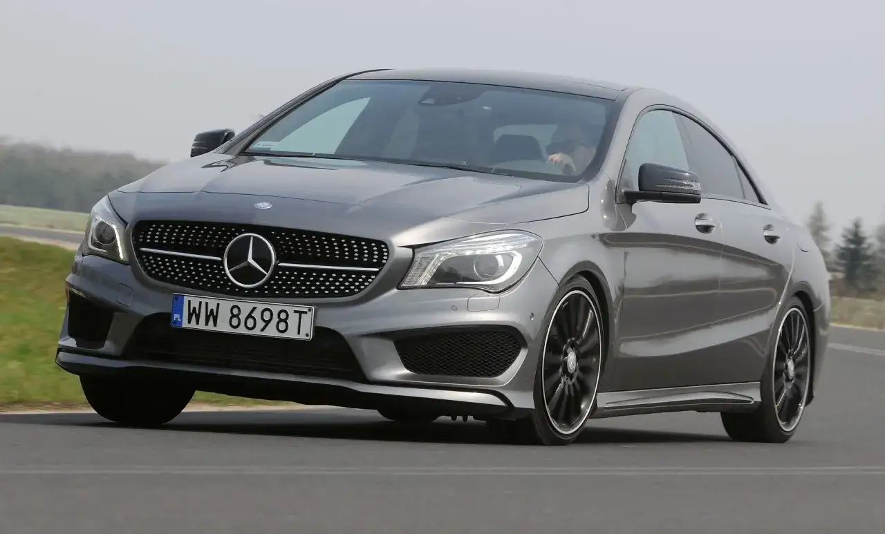 Szary Mercedes CLA 180 na drodze, z kierowcą w okularach przeciwsłonecznych za kierownicą.