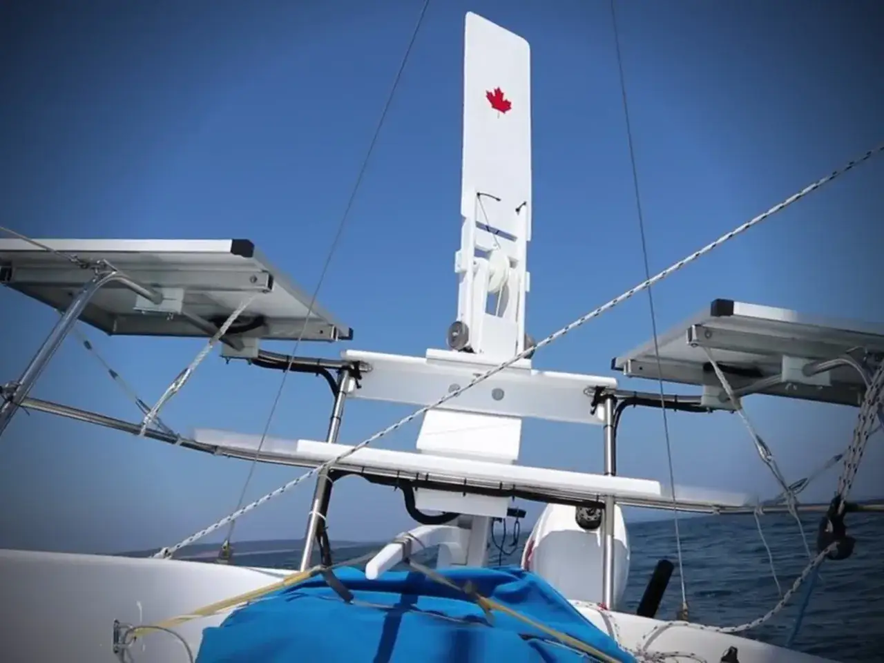 Weiße Windfahne mit kanadischer Flagge auf einem Segelboot, mit Solarpaneelen und dem blauen Himmel im Hintergrund.