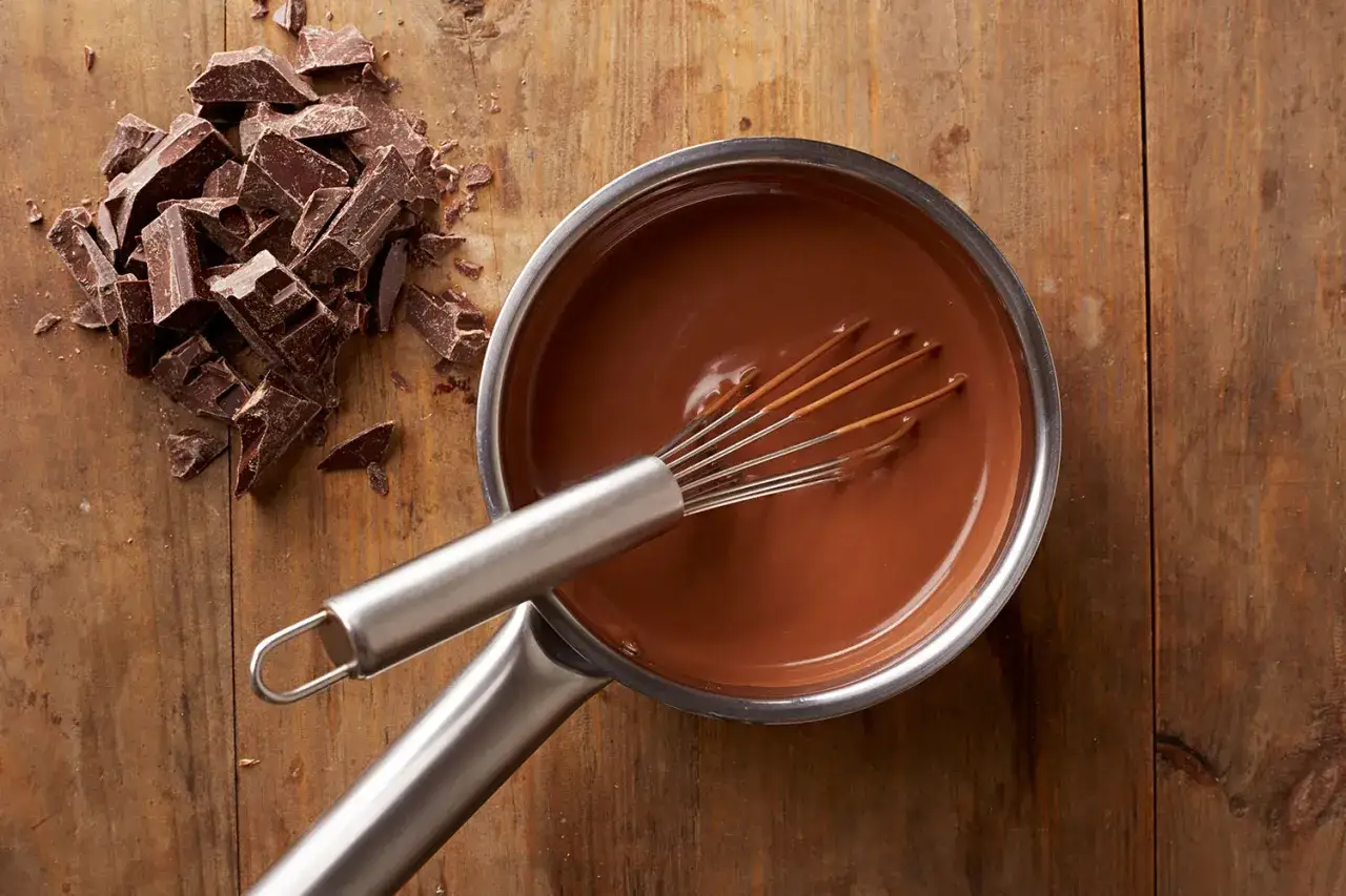 Chocolat fondu qui durcit dans une casserole, avec des morceaux de chocolat à côté sur une planche en bois.