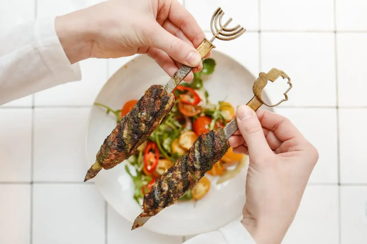 Dwie porcje soczystego mięsa wołowego kebab na patyczkach, podane z sałatką z pomidorków i papryczki chili.