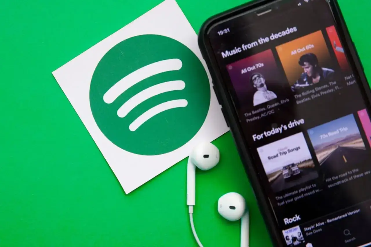 Logo Spotify, smartfon z aplikacją muzyczną i słuchawki na zielonym tle.