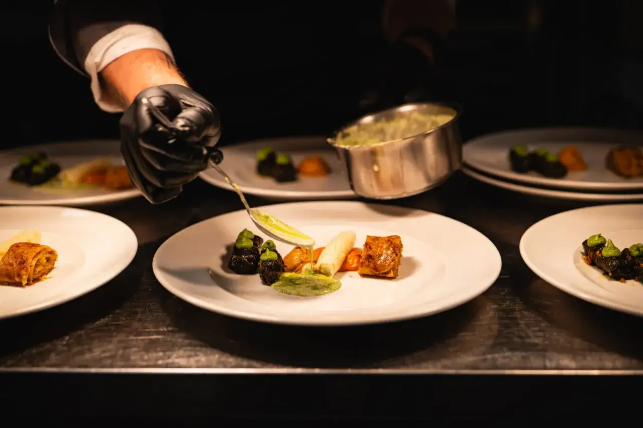 Szef kuchni precyzyjnie serwuje sos, dbając o zasady serwowania dań w stylu "fine dining" na dużych imprezach.