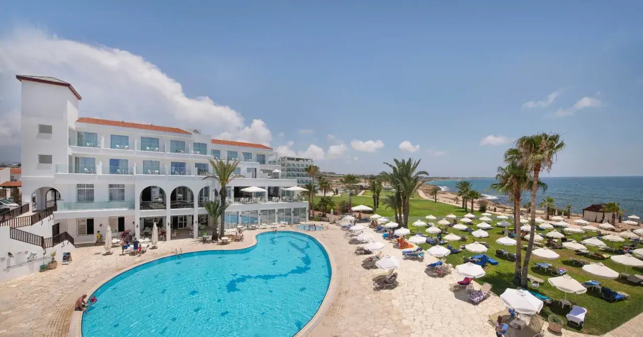 Słoneczny dzień w Akti Beach Village Resort. Basen, leżaki, palmy i morze - idealne miejsce na wakacje.