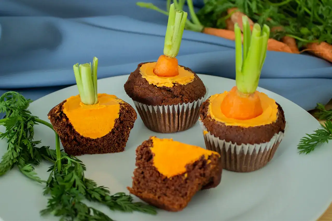 Schokoladen-Muffins mit orangefarbener Glasur und einem kleinen Karottenstück mit Grün als Osterdekoration.