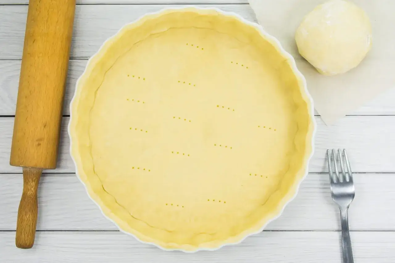 Pâte à tarte à la casserole prête à être garnie, avec une boule de pâte, un rouleau et une fourchette.