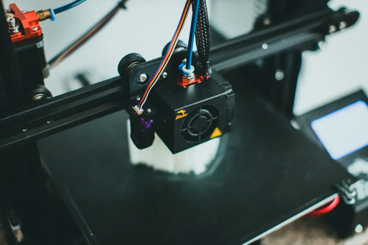 Zbliżenie na głowicę drukarki 3D drukującą biały obiekt.