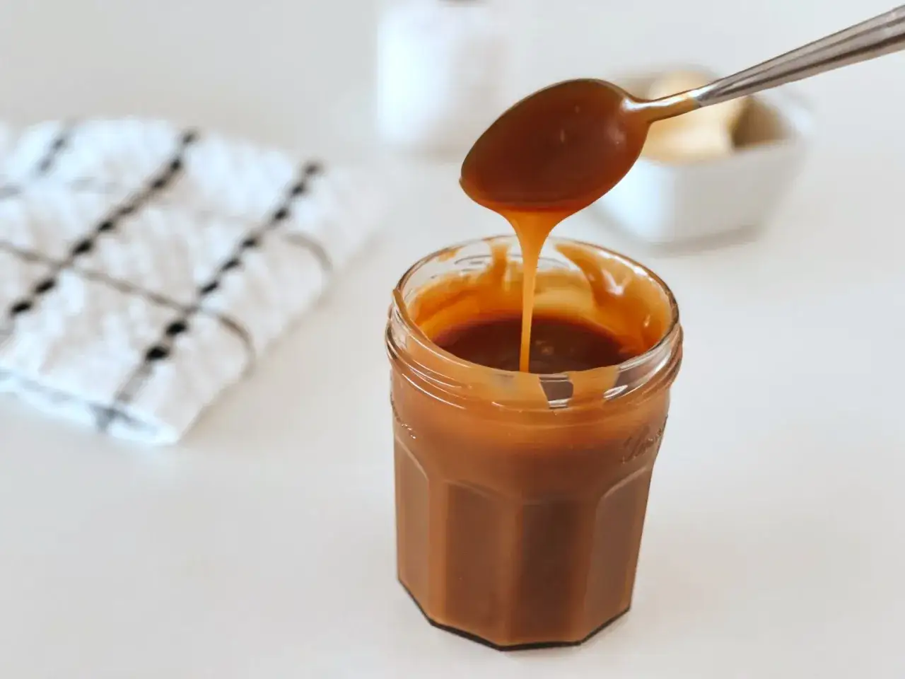 Une cuillère verse un caramel beurre salé liquide dans un pot en verre. Parfait pour une recette gourmande.