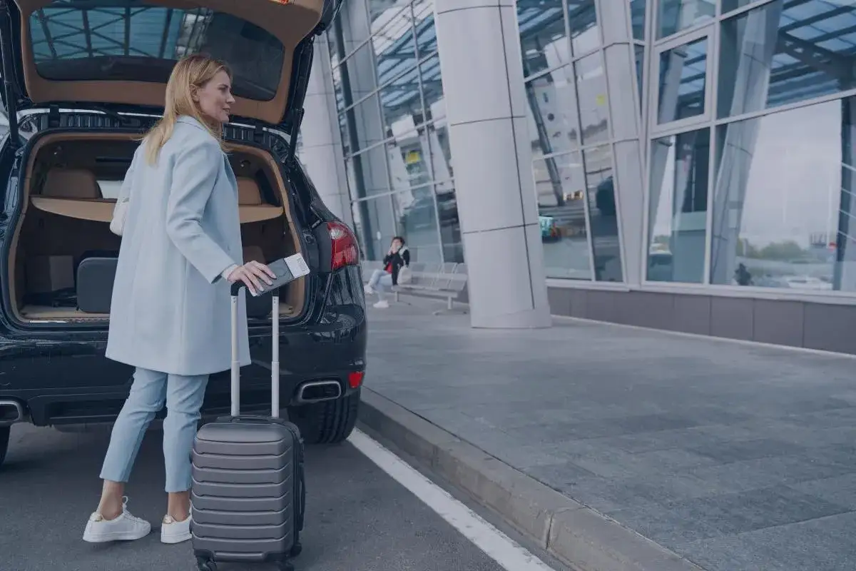 Kobieta z walizką i paszportem przy samochodze. Dojazd z lotniska do hotelu jako czas pracy, zasady z orzecznictwa sądu.