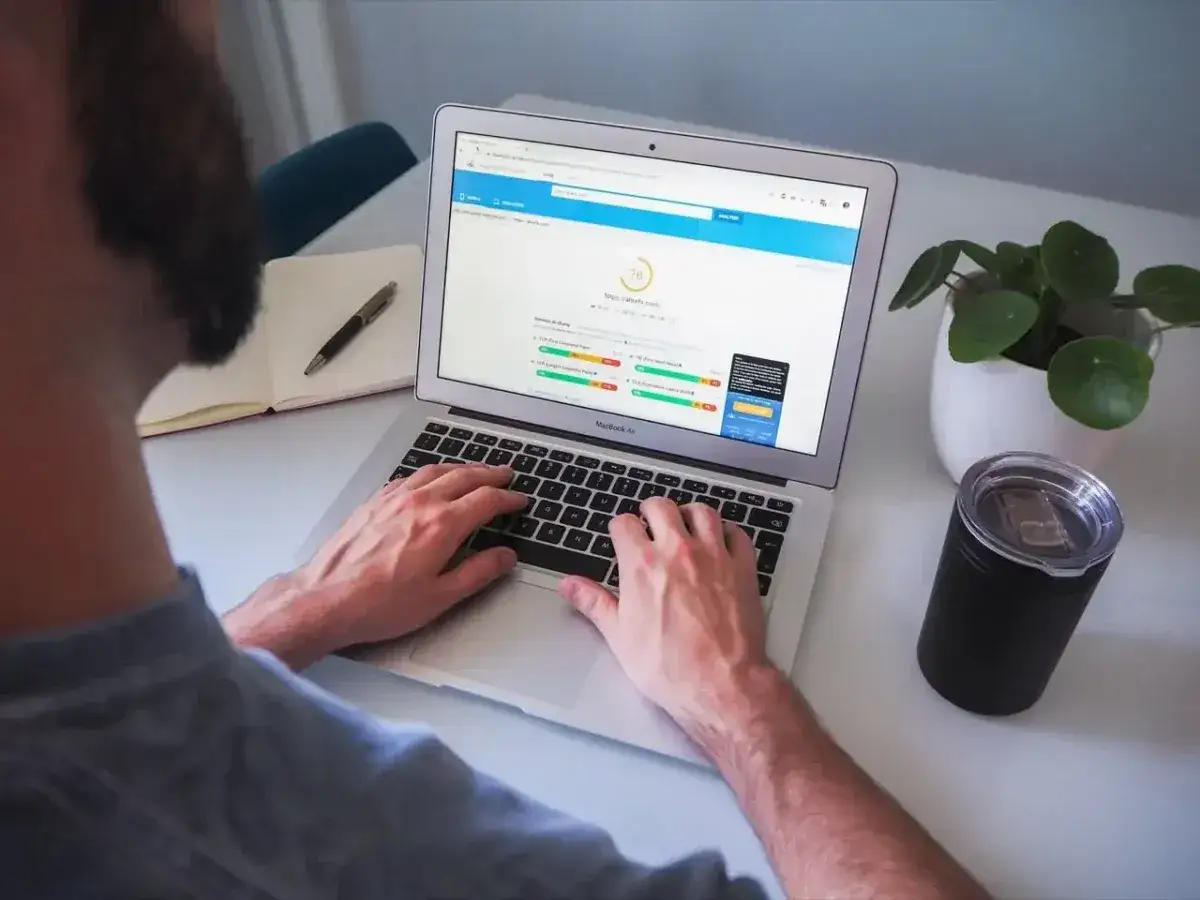 Osoba pracuje na laptopie, na ekranie którego widoczny jest wynik testu prędkości strony internetowej.