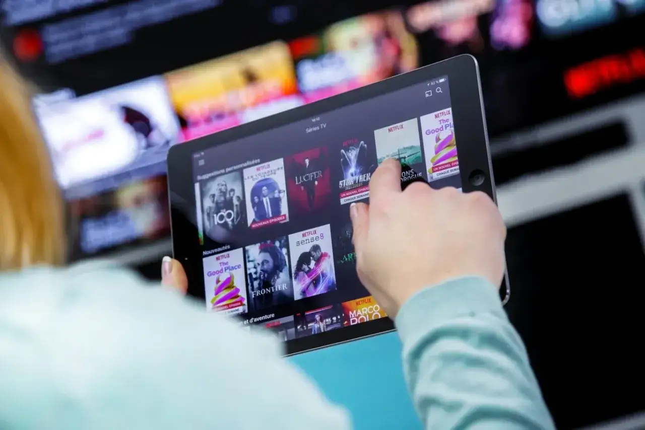 Osoba przegląda seriale na tablecie, szukając sposobu, jak pobrać serial z Netflixa na komputer.