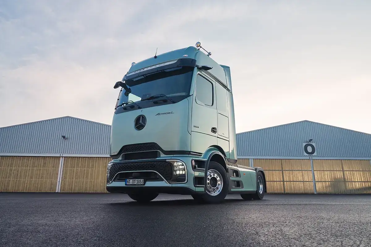 Nowy Mercedes Actros MP4 w kolorze miętowym, zaparkowany przed halami magazynowymi.