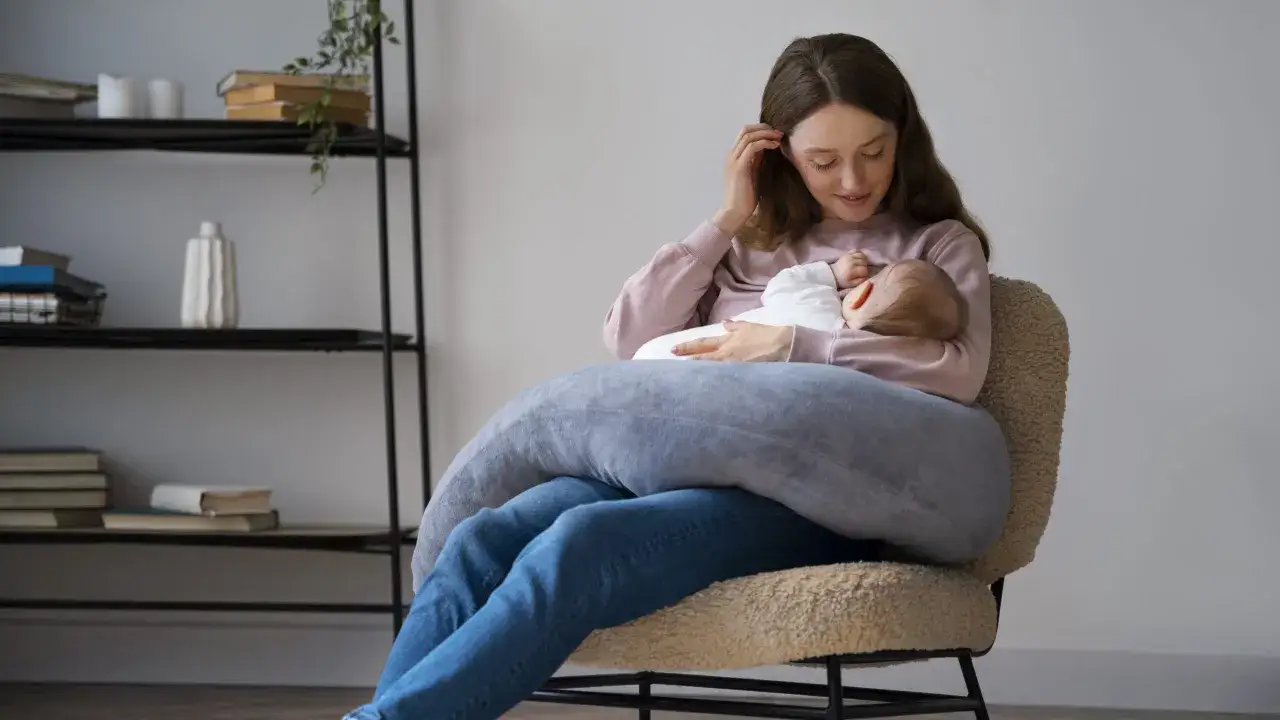 Szukasz idealny fotel do karmienia? Młoda mama z dzieckiem na rękach, otulona poduszką, siedzi na wygodnym, pluszowym fotelu.