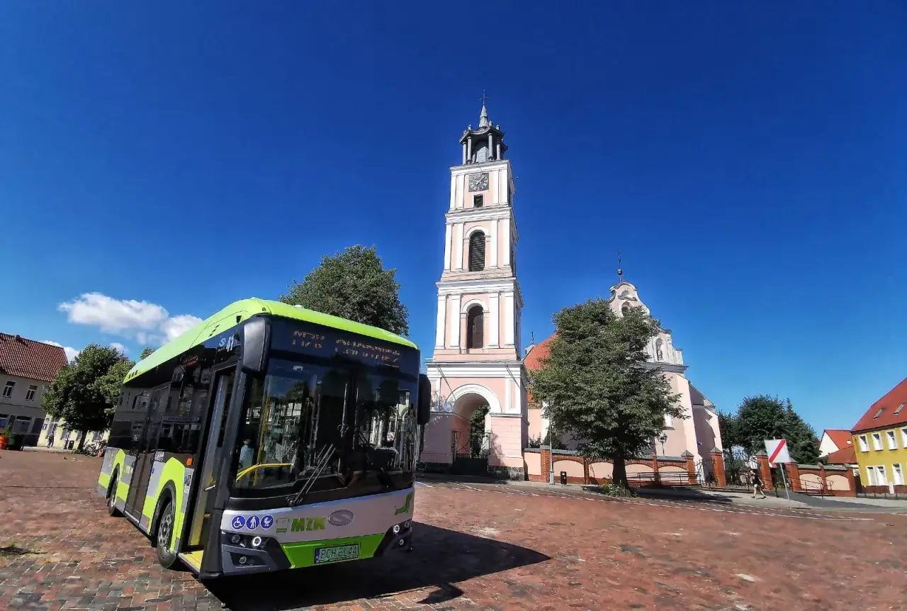 Zielony autobus MZK Chodzież czeka na pasażerów pod wieżą kościoła. Sprawdź mzk chodzież rozkład jazdy i zaplanuj podróż!