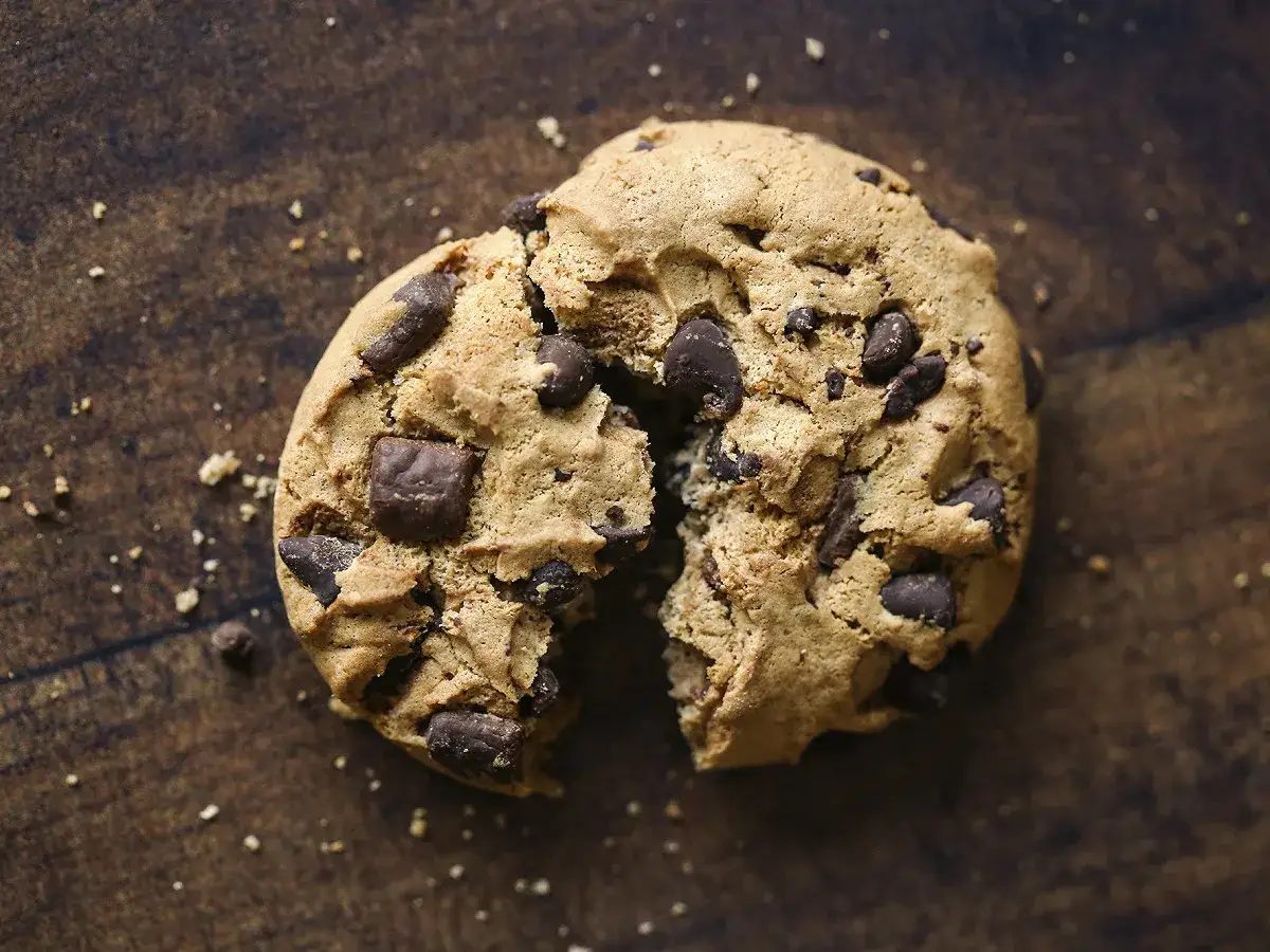 Un cookie aux pépites de chocolat, brisé en deux, révèle sa texture moelleuse. La meilleure recette de cookies pour un goûter gourmand.
