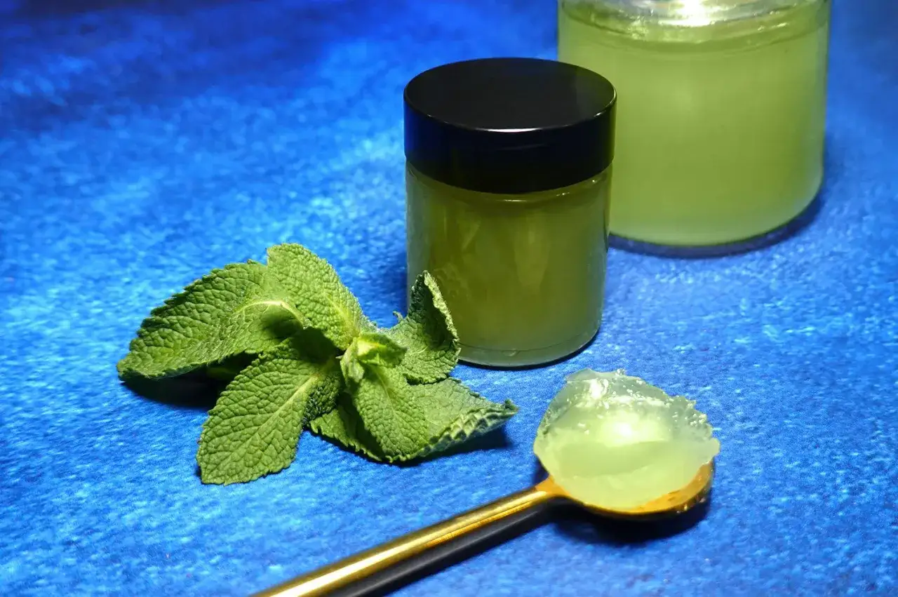 Une cuillère dorée présente une portion de gelée de menthe fraîche. À côté, un pot fermé et un autre ouvert contiennent cette même gelée verte et rafraîchissante.