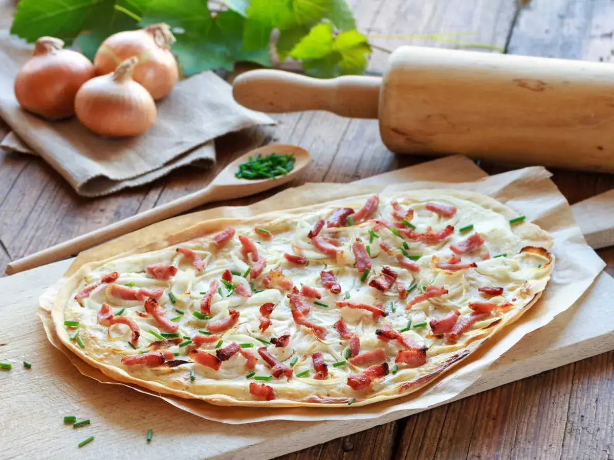 Flammekueche prête à être dégustée, avec ses oignons, lardons et ciboulette. Une recette facile pour un repas convivial.