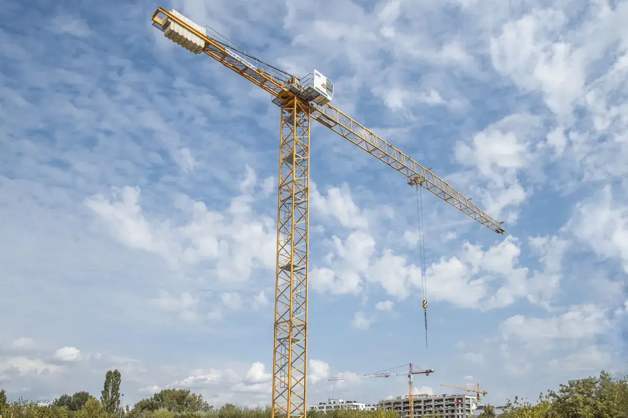 Żółty dźwig budowlany na tle błękitnego nieba z chmurami. Zastanawiasz się, ile zarabia operator dźwigu?