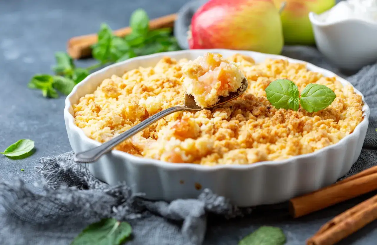 Une cuillère prélève une bouchée dorée de ce meilleur crumble aux pommes, garni de feuilles de menthe fraîche.
