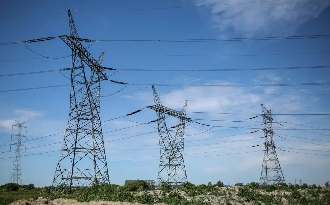 Wysokie wieże energetyczne z przewodami na tle błękitnego nieba z chmurami.
