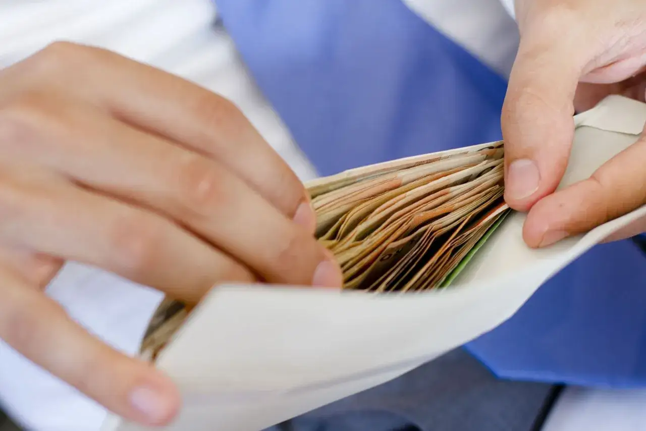 Dłonie wkładają plik banknotów do koperty. Zastanawiam się, ile na wesele od chrzestnej.