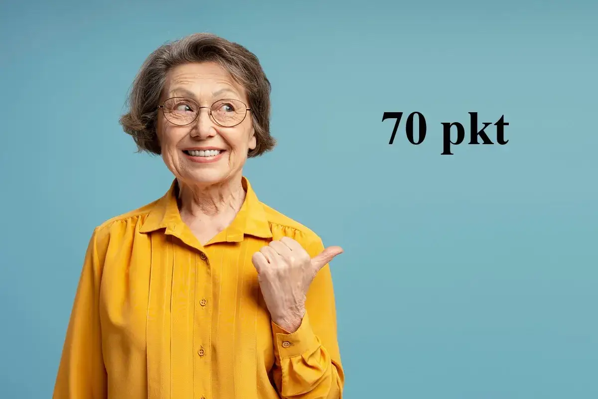 Uśmiechnięta starsza pani w żółtej bluzce wskazuje kciukiem na napis "70 pkt", sugerując świadczenie wspierające punkty.