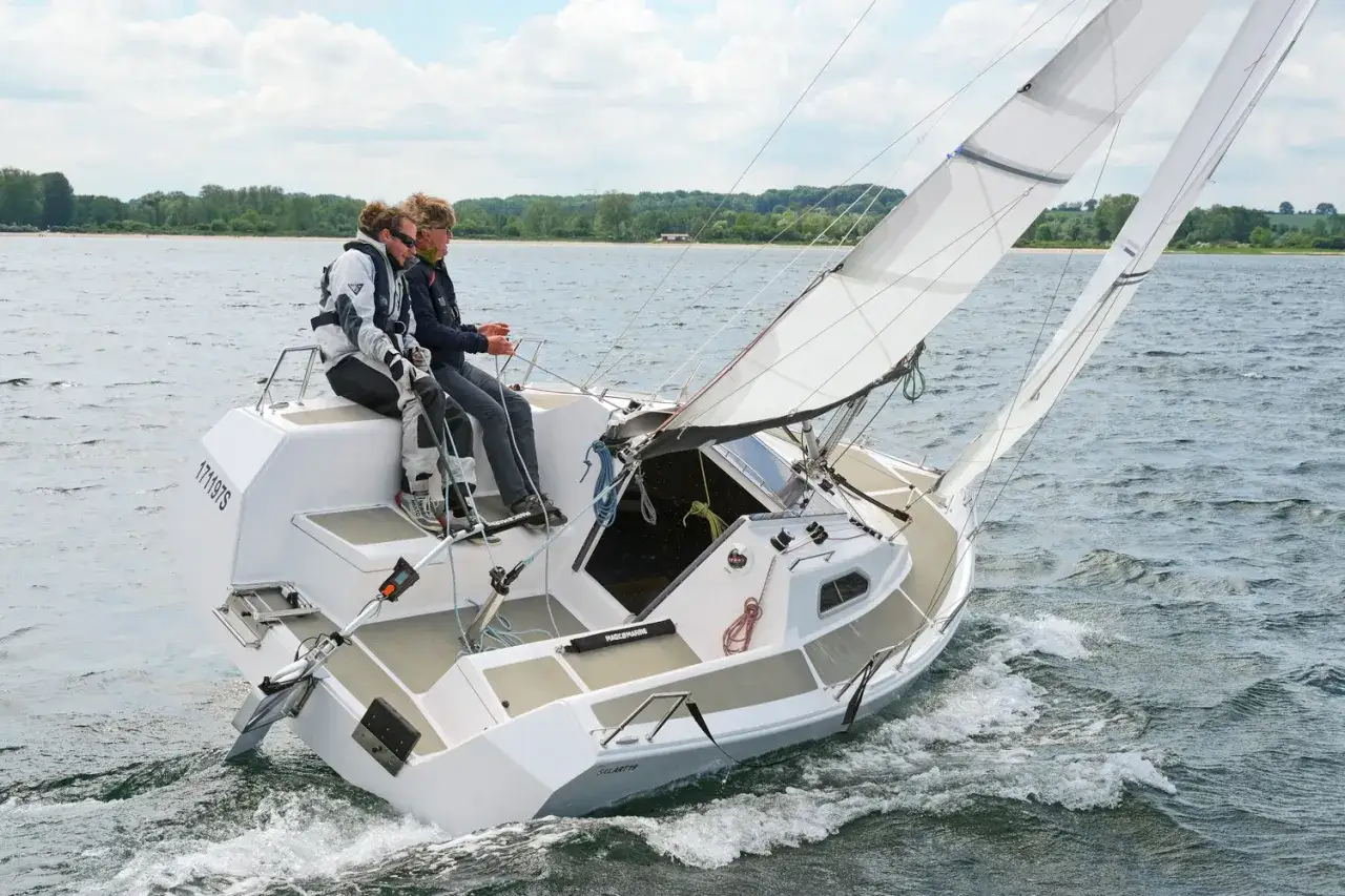 Zwei Segler genießen eine Fahrt auf einer Sailart 20. Das Boot gleitet durch das Wasser, die Segel sind gesetzt.