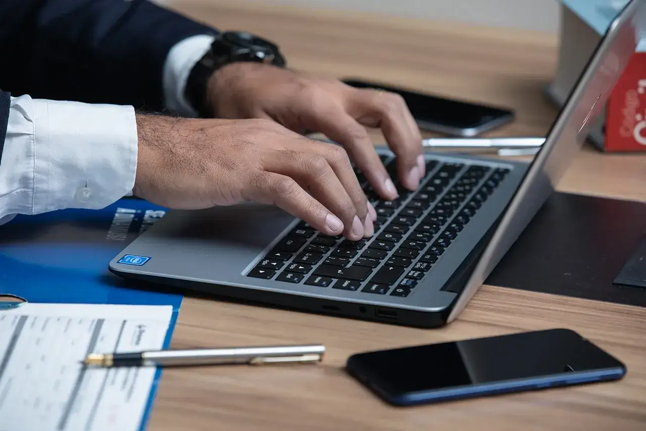 Prawnik pisze na laptopie, szukając informacji, jak napisać apelację od wyroku karnego wzór. Na biurku leżą dokumenty i telefon.