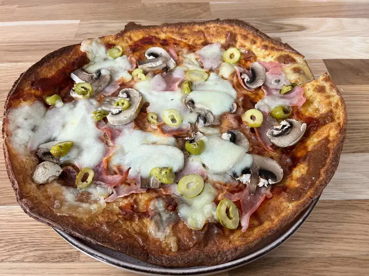 Apetyczna pizza z twarogu z pieczarkami, szynką i oliwkami, z ciągnącym się serem.