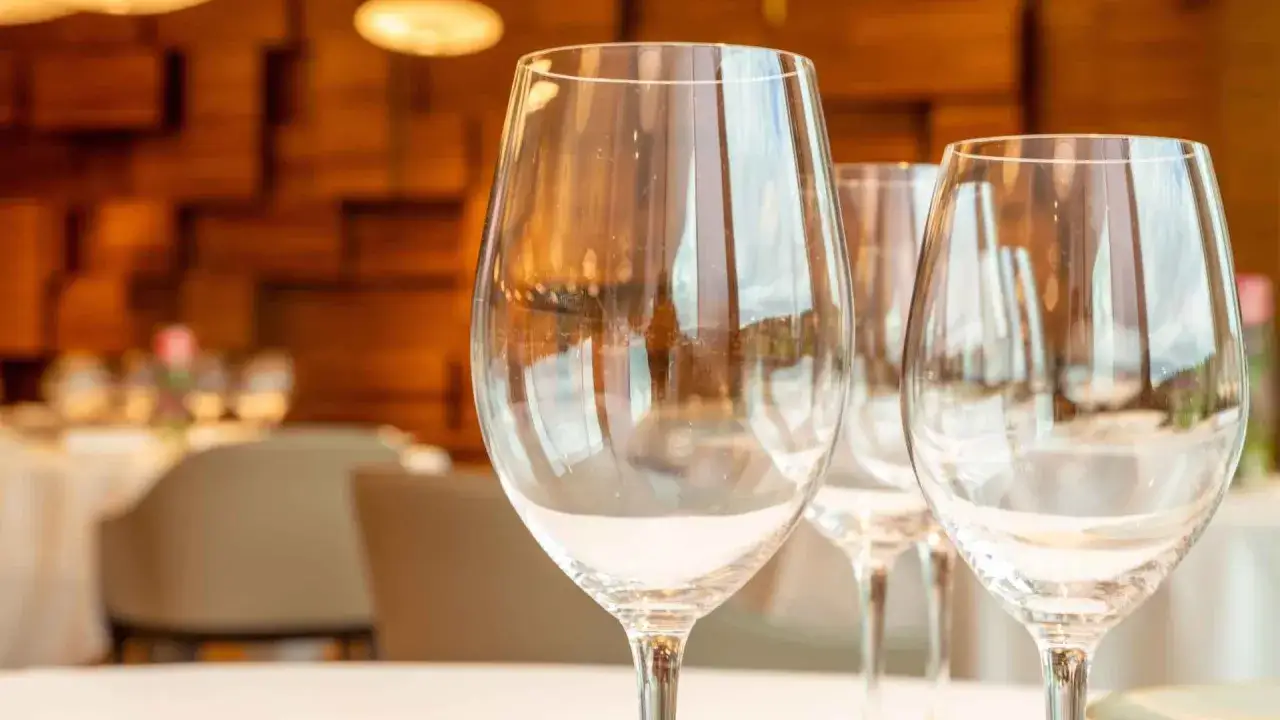 Trois verres à vin vides, prêts pour un repas gastronomique. La position des verres à la française suggère une table élégamment dressée dans un restaurant chaleureux.