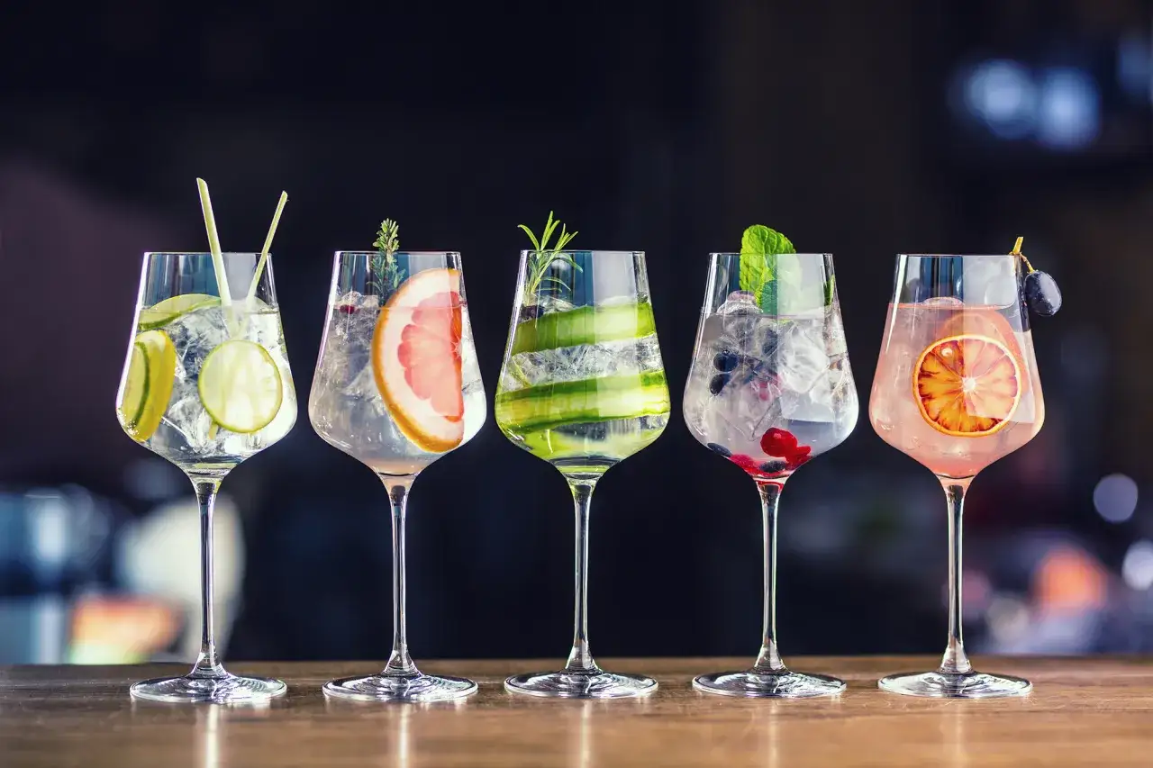 Pięć drinków z wódką i ginem, ozdobionych owocami i ziołami, na eleganckim tle.