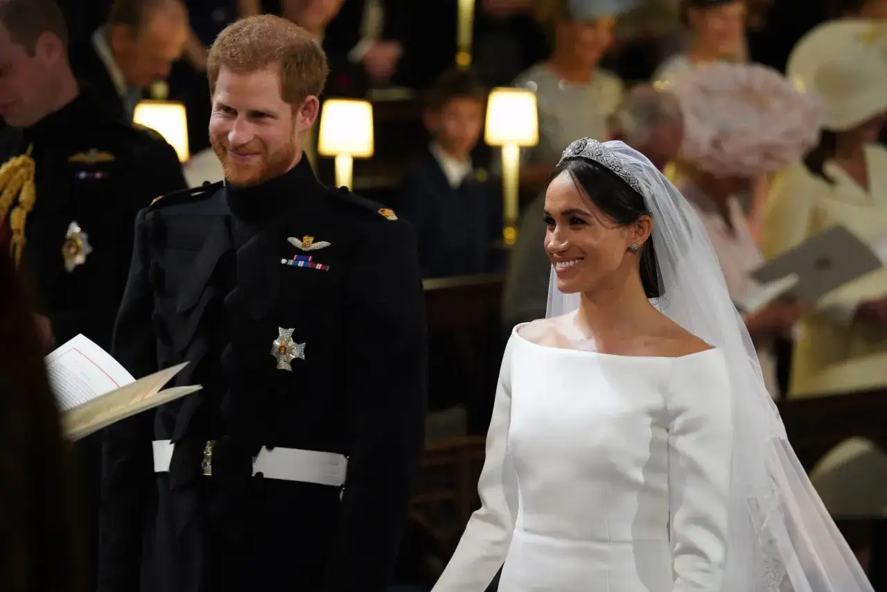 Meghan Markle y el Príncipe Harry sonríen en su boda. Ella luce un vestido blanco y él un uniforme militar.