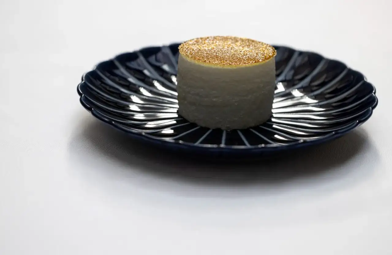 Un cylindre blanc, saupoudré d'or, sur une assiette bleue. Une idée de quoi manger à Paris pour une expérience culinaire unique.
