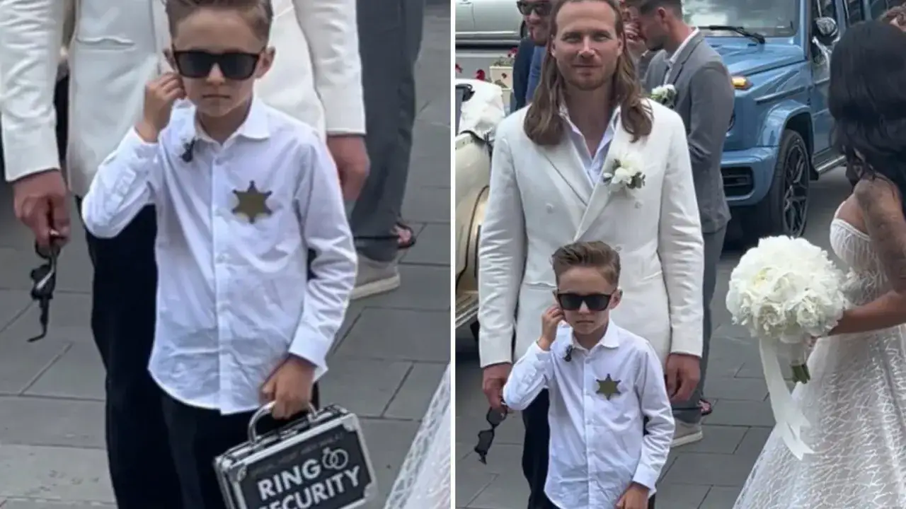 Chłopiec w okularach przeciwsłonecznych, z odznaką i walizką "Ring Security", niesie obrączki do ślubu.