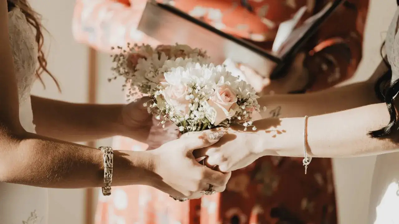 Manos entrelazadas sosteniendo un ramo de flores, un momento íntimo de los rituales boda civil.