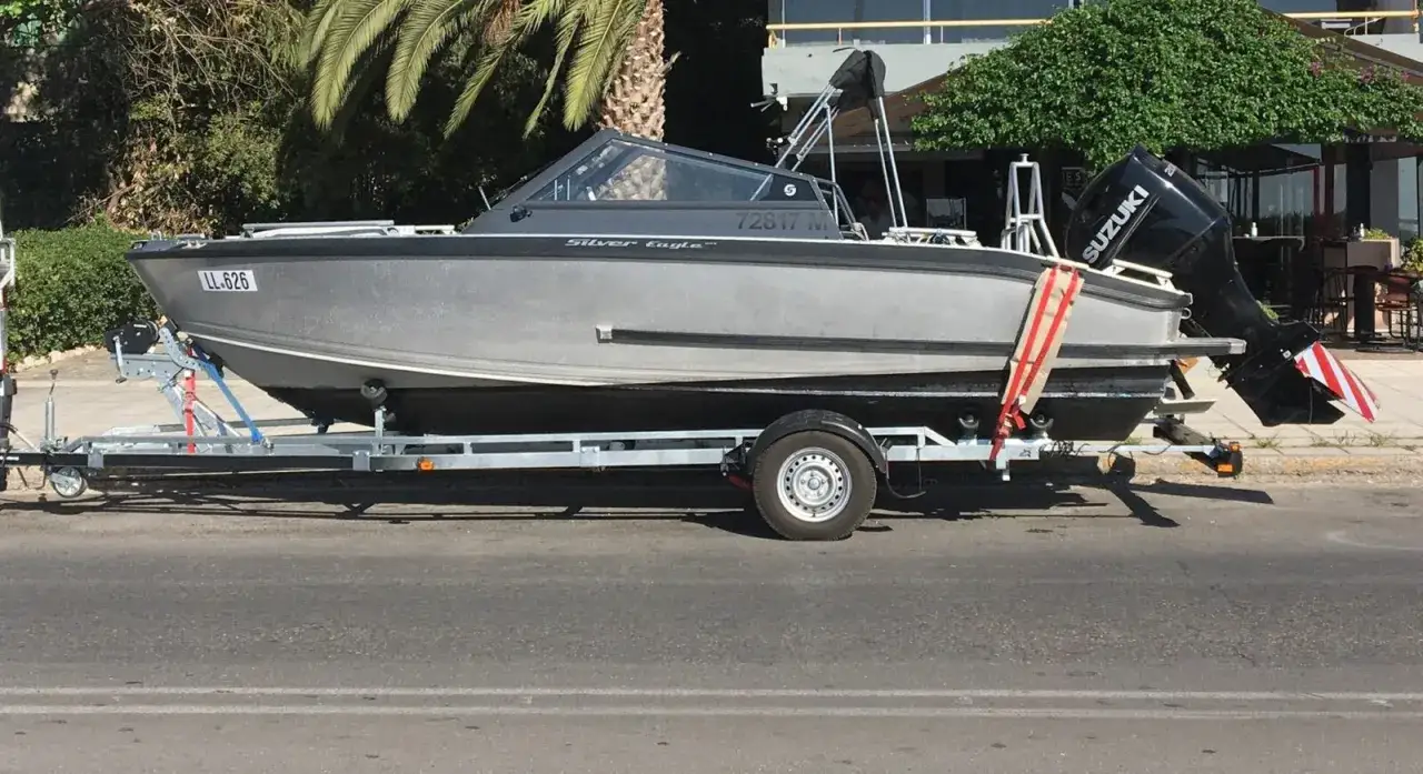Ein graues Boot, "Silver Eagle", wird auf einem Anhänger transportiert. Der Suzuki Außenbordmotor ist montiert.