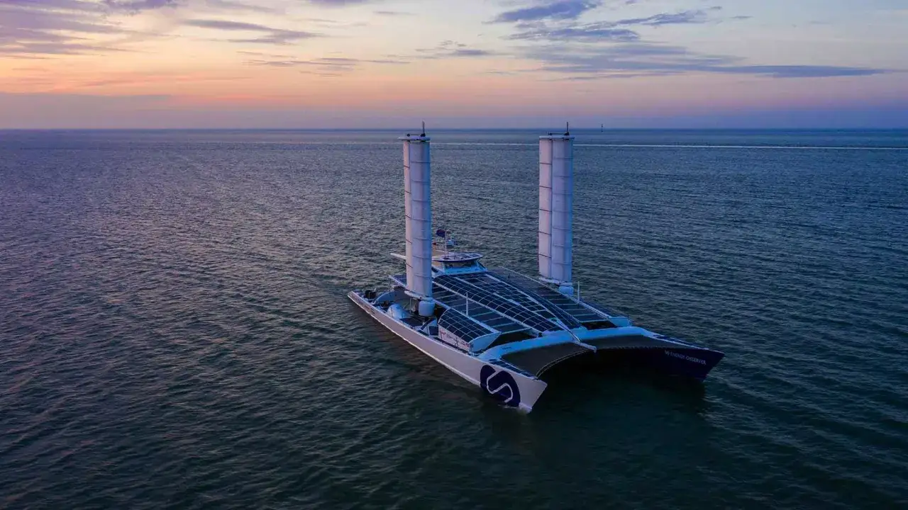 Der ENERGY OBSERVER, ein futuristisches Schiff mit Solarpaneelen und Windturbinen, gleitet bei Sonnenuntergang über das Meer.
