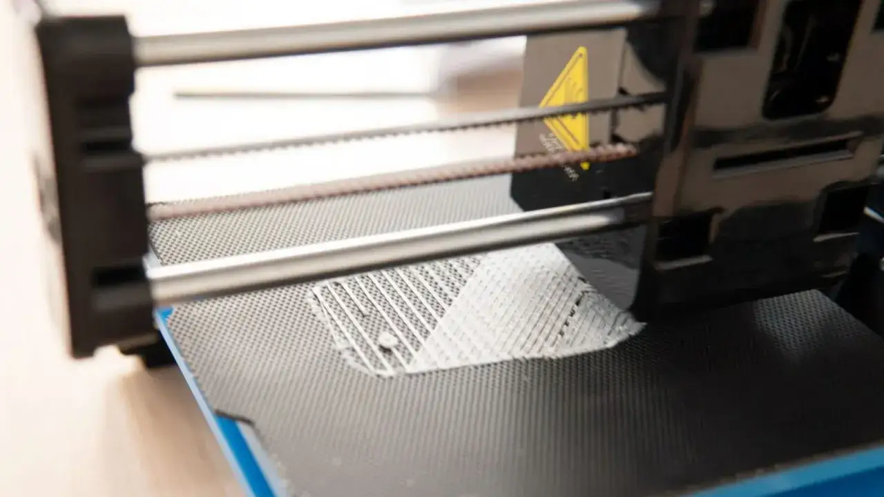 Drukarka 3D drukuje biały, siatkowy obiekt na czarnej platformie.