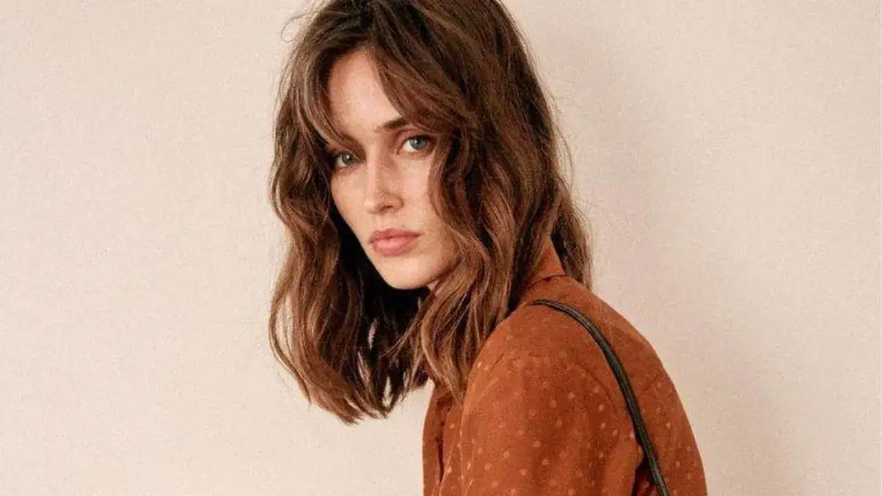 Mujer con un corte de pelo clavicut, ondas suaves y flequillo desfilado, luciendo un top marrón con lunares.