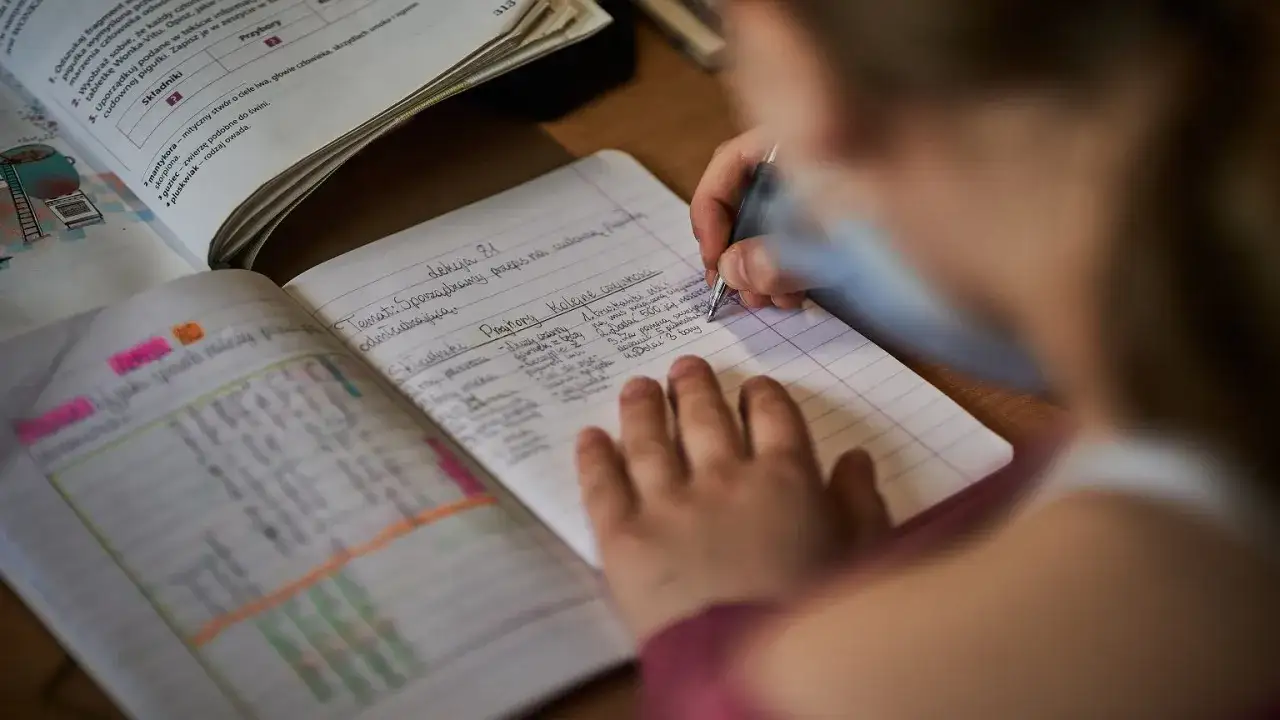Dziecko pisze w zeszycie, co może być podstawą do oceny przez nauczyciela.