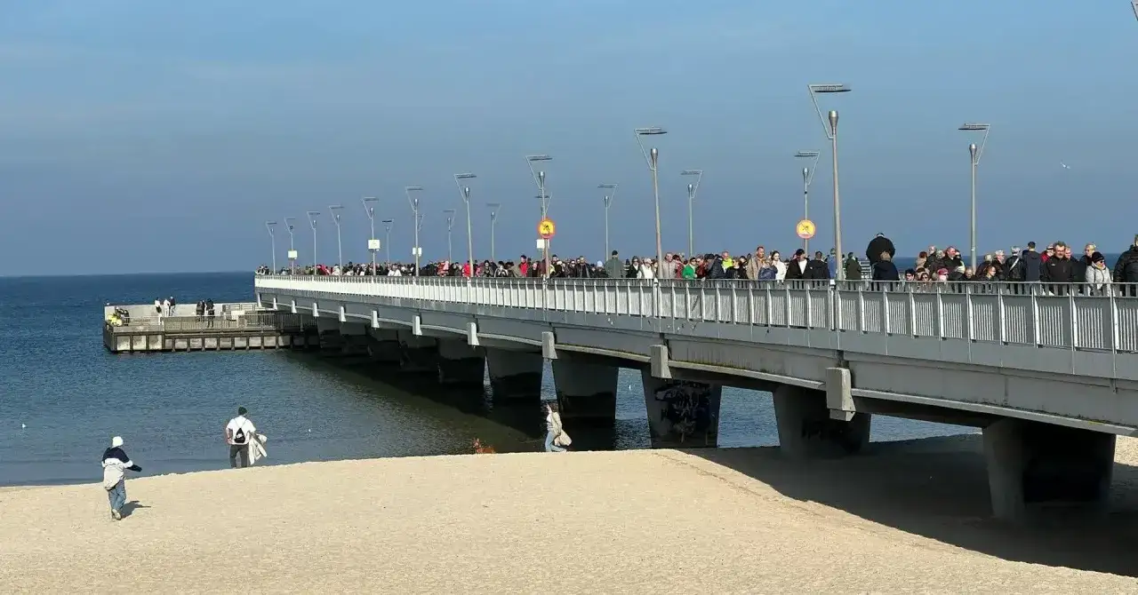 Tłum ludzi spaceruje po molo w Kołobrzegu. Czy molo w Kołobrzegu jest płatne? Tego nie widać na zdjęciu, ale widok jest piękny.