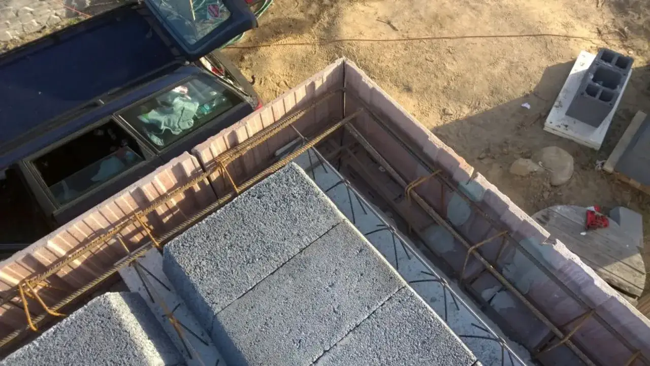 Budowa stropu ackermana w toku. Betonowe pustaki i zbrojenie czekają na zalanie betonem. Obok stoi samochód.