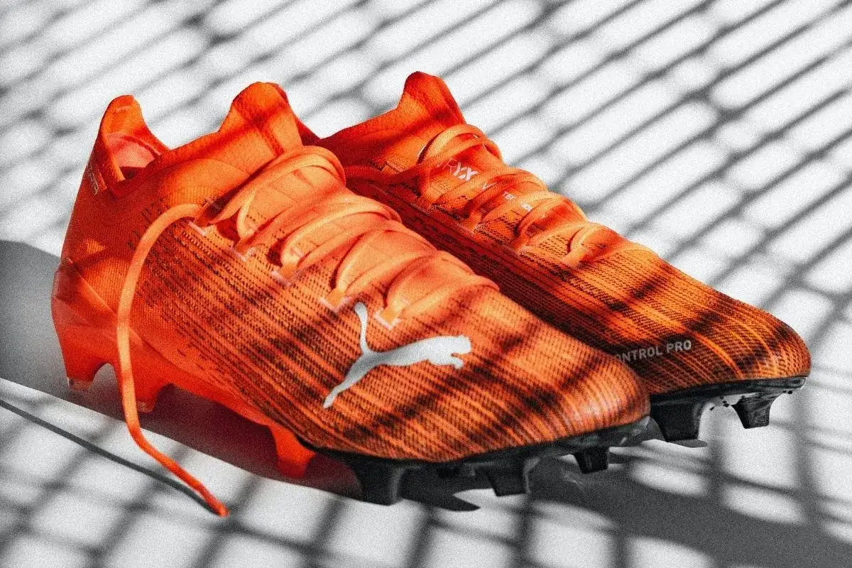 Pomarańczowe korki piłkarskie Puma z napisem "CONTROL PRO". Różnice między korkami profesjonalnymi a amatorskimi są widoczne w technologii i materiałach.