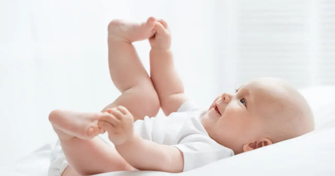 Uśmiechnięte dziecko leży na plecach, podnosząc nóżki. Czas na zmianę pampersów na większe, gdy maluch rośnie.
