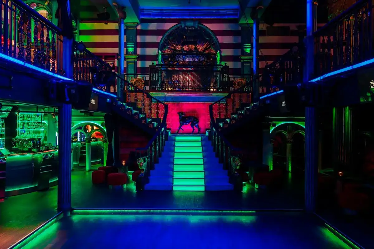 Wnętrze klubu Teatr Capitol nocą, oświetlone neonami. Centralnie umieszczone schody prowadzą do górnej galerii.