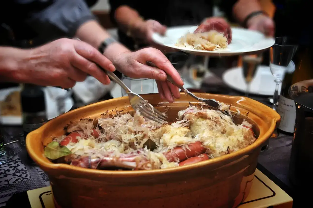 Un plat généreux de choucroute garnie, spécialité de la gastronomie alsacienne, est servi. Des mains servent ce délice, promesse d'une savoureuse nourriture d'Alsace.